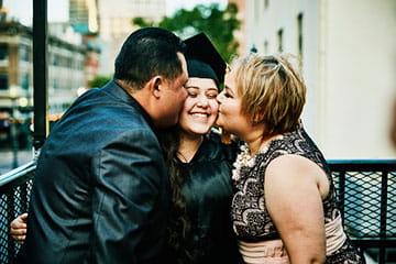 年轻女子在毕业典礼上微笑着，她的父母亲吻她的脸颊